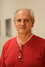 Porträt einer Person mit kurzem, grauem Haar und roter Kleidung.