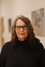 Person mit Brille und dunklem Haar, porträtiert vor einem hellen Hintergrund. Freundlicher Gesichtsausdruck.