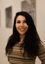 Person mit dunklen langen Haaren und gemustertem Pullover lächelt freundlich in die Kamera.