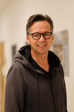 Person mit dunklem Hoodie und Brille lächelt in die Kamera.