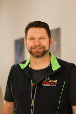 Porträt einer Person mit kurzem, dunklem Haar und Bart, bekleidet mit einem sportlichen Outfit und einer Weste.