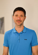 Person mit kurzem, dunklem Haar und blauem Polohemd schaut freundlich in die Kamera.