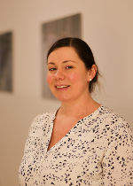 Person mit gelocktem Haar und freundlichem Blick. Trägt ein gemustertes Oberteil.