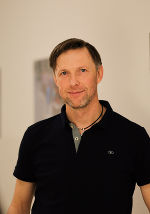 Person mit kurzbraunem Haar und dunklem Polohemd schaut freundlich in die Kamera.