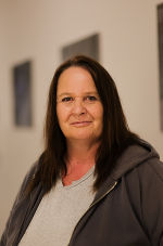 Person mit dunklen Haaren und grauer Jacke schaut freundlich in die Kamera.