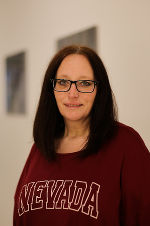 Person mit dunklen Haaren und Brille trägt ein rotes Sweatshirt mit Aufschrift.