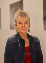 Person mit rotem Oberteil und blauer Jacke, lächelnd in die Kamera blickend.